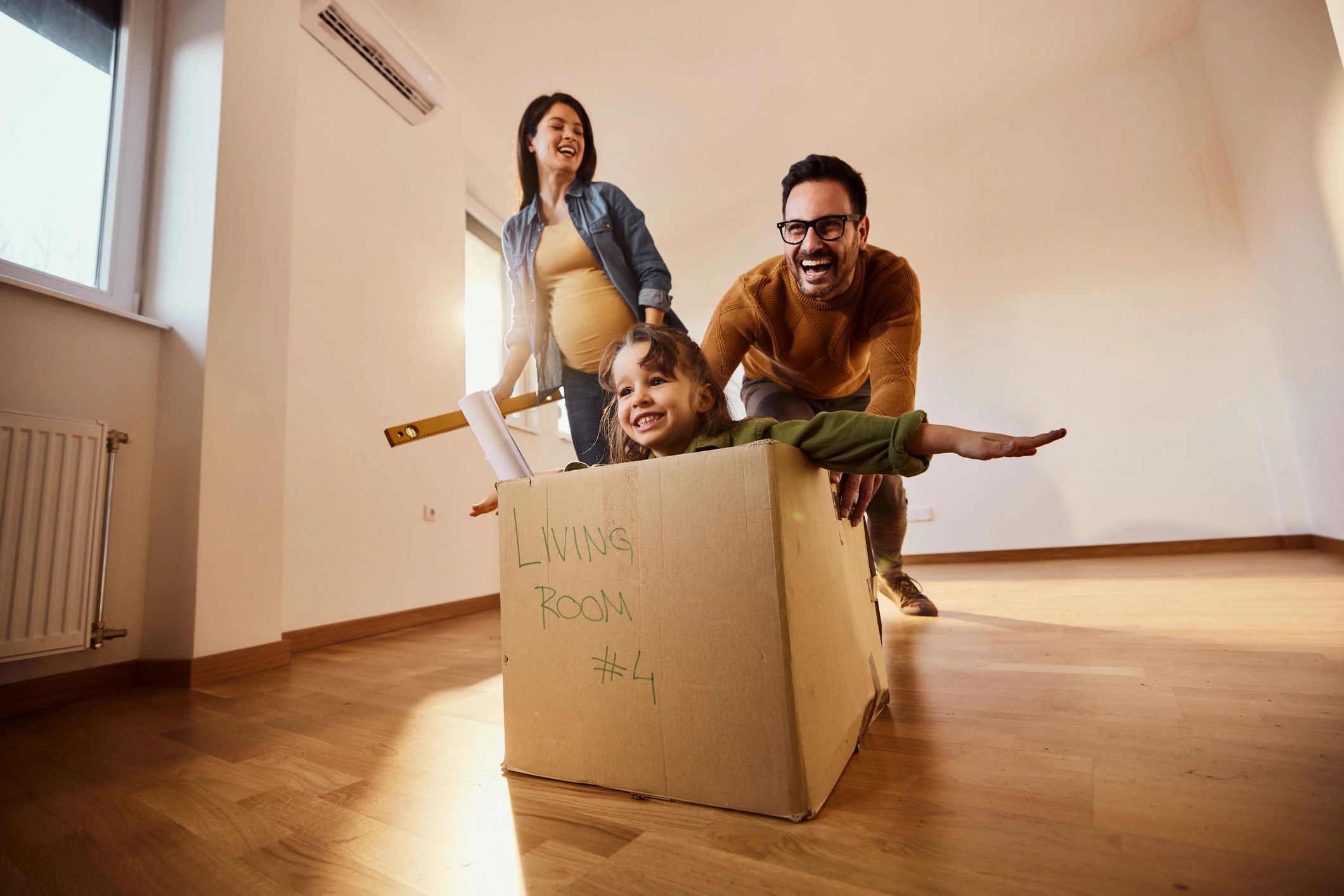 Family enjoying playful time with child in a cardboard box indoors.
