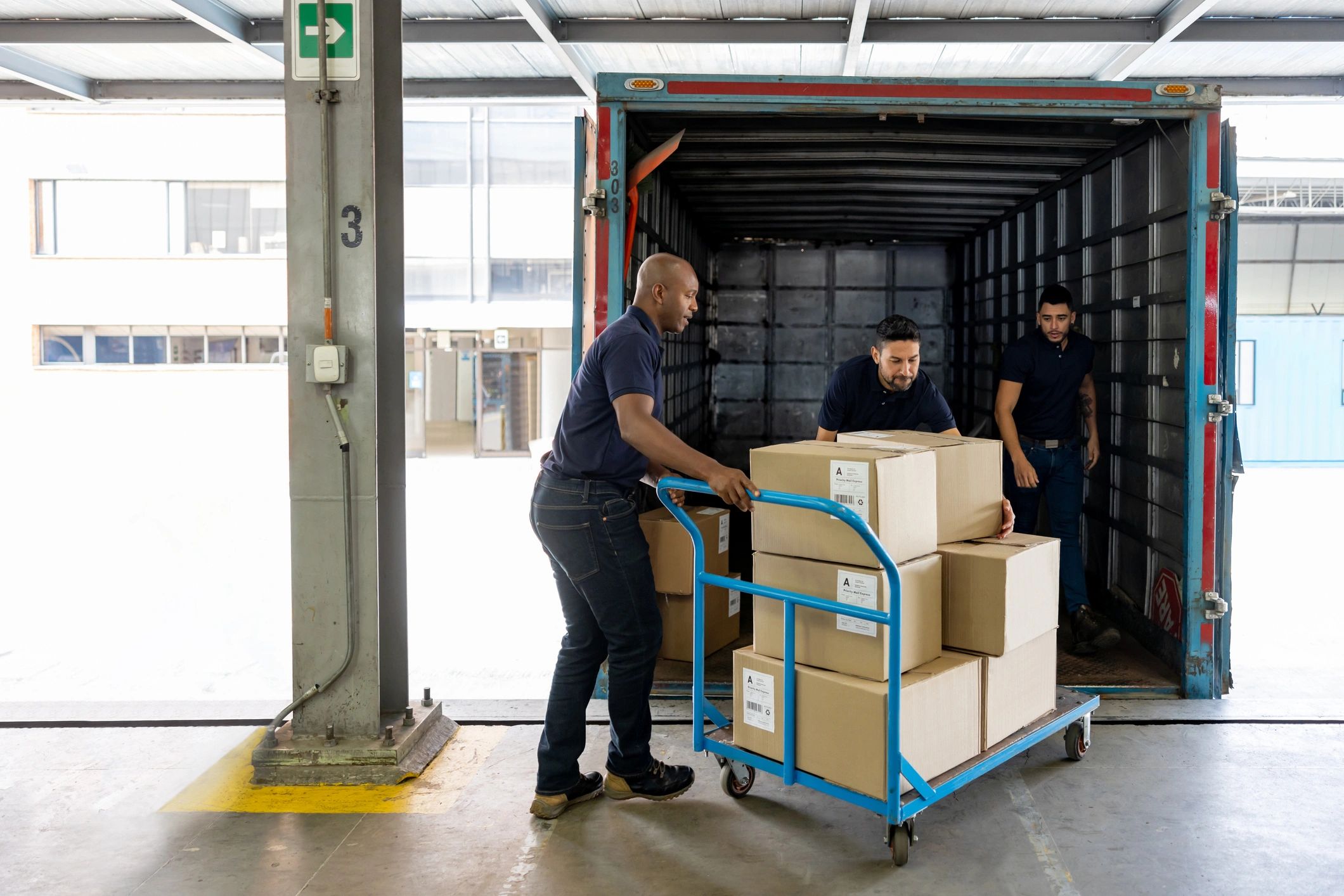 Workers loading boxes into a truck using a cart.