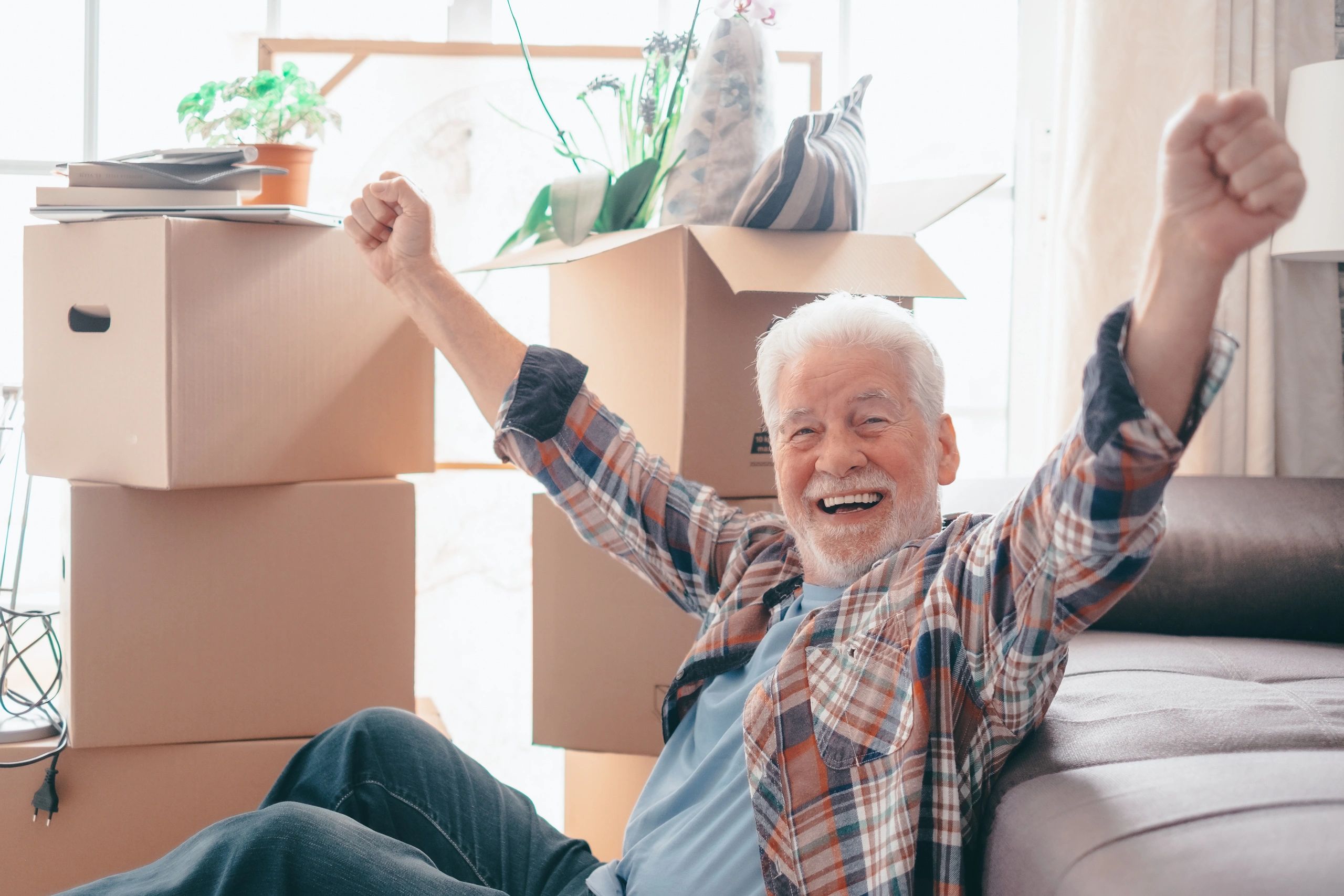 Happy elderly man celebrating in a new home surrounded by moving boxes.