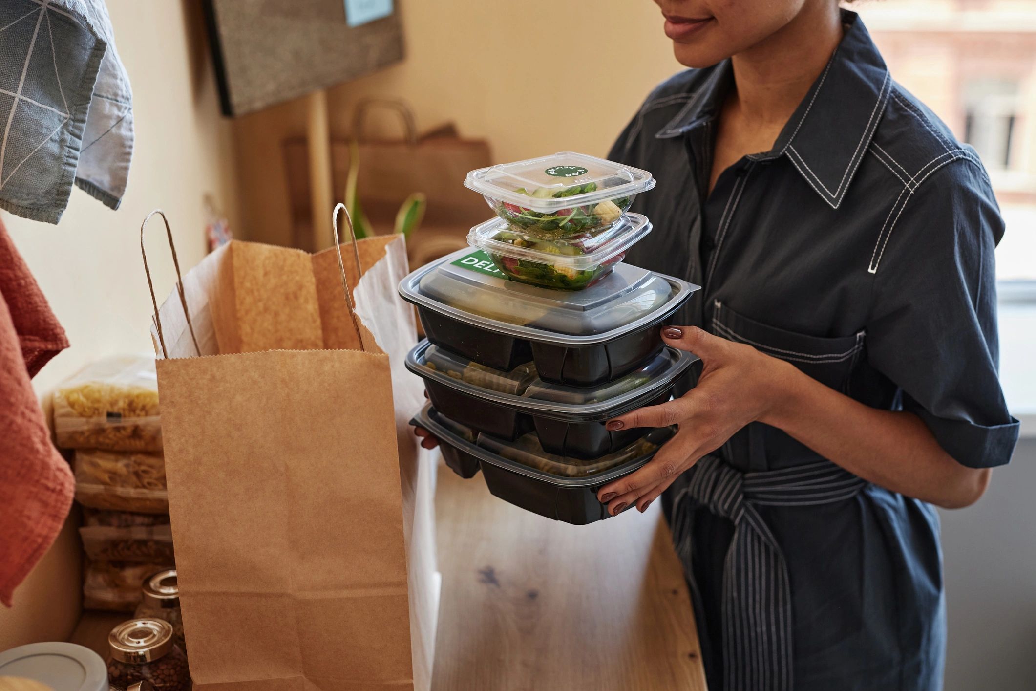 Person holding a stack of black plastic food containers indoors.