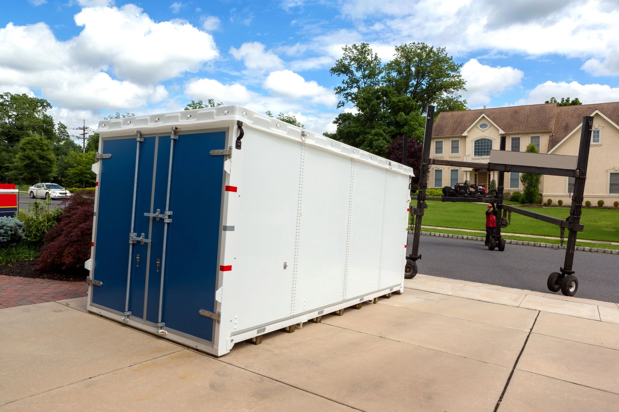 A large white storage container with blue doors on a driveway.