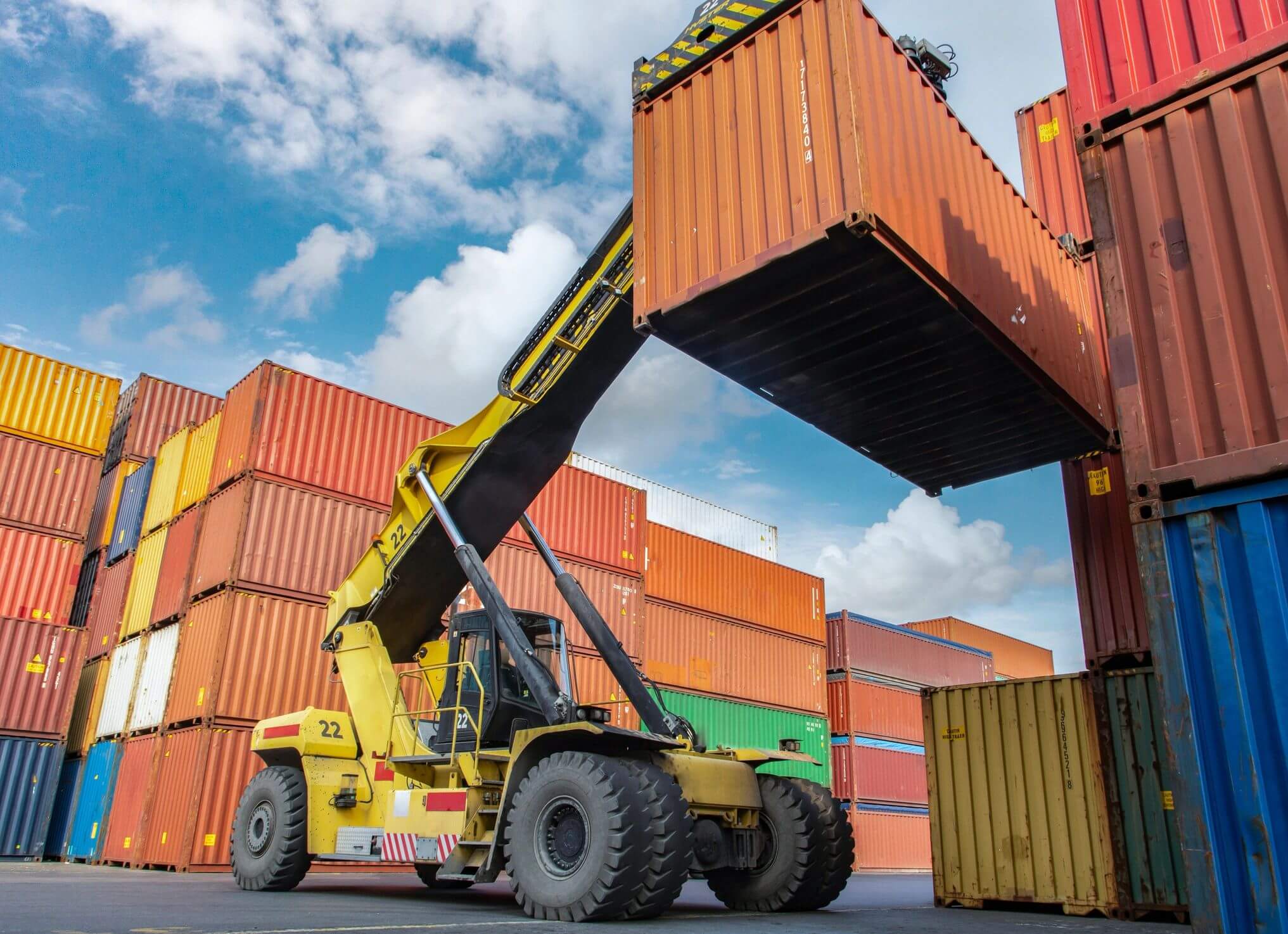 A forklift lifts a shipping container in a busy port area.