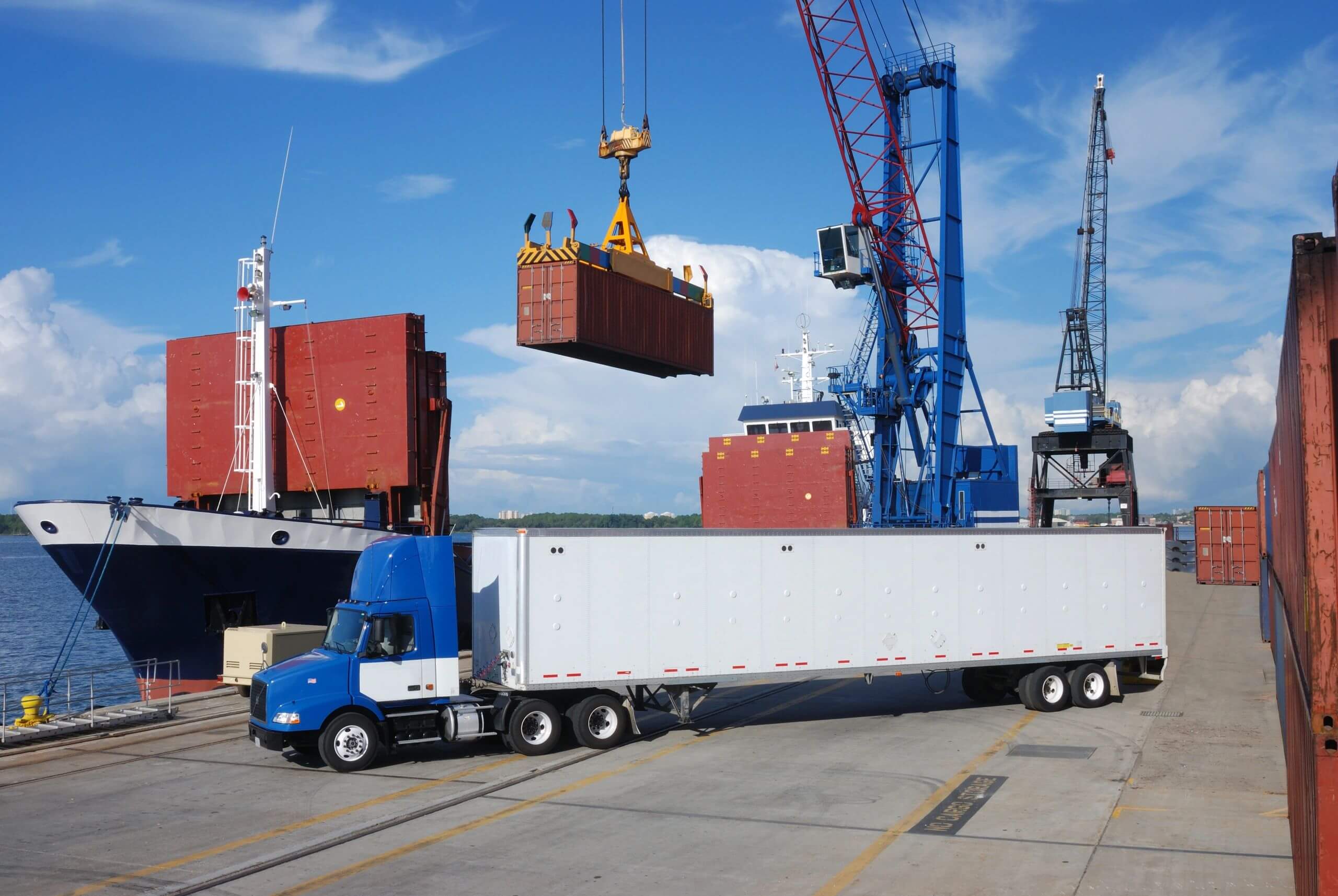 A container is being loaded onto a truck at a busy port.